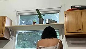 Latina milf enjoys washing dishes in the kitchen with a smile.