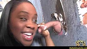 An ebony woman in the USA performs an interracial gloryhole blowjob, sucking a big black cock through the hole