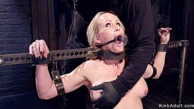 Gagged blonde locked in metal stock for rough bondage