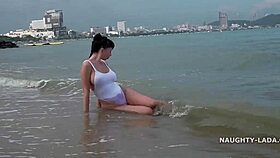 Milf wears see-through swimsuit on wet beach.